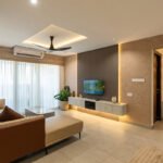 Modern minimalist living room with a neutral color palette, featuring a floating TV unit, recessed cove lighting, and a beige L-shaped sofa.